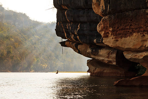 The Manambolo river gorge with a dramatic overhanging limestone cliff and a lone pirogue in the distance
